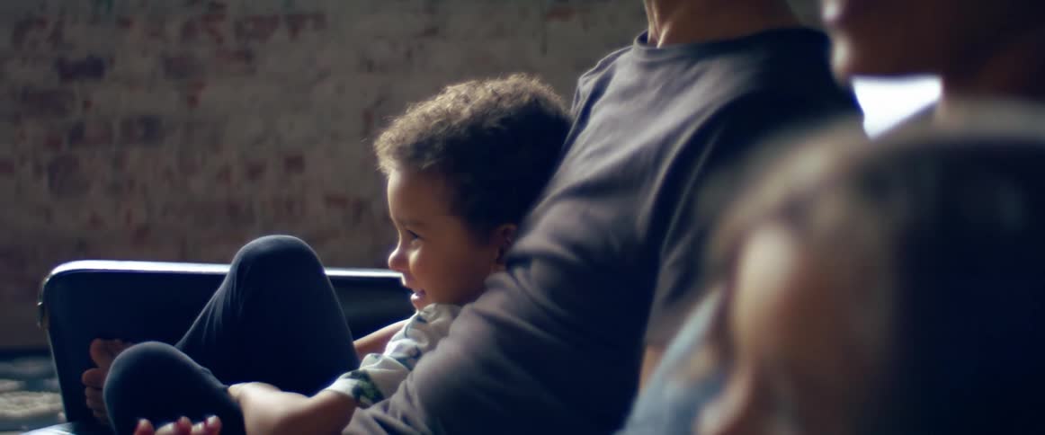 Parents with their children sitting side by side on the sofa watching television
