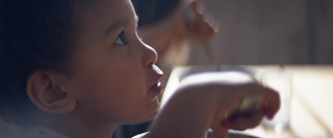 A toddler boy eating food from a bowl at a dining table