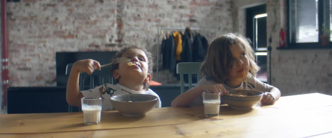 Two brothers sit on chairs at a table eating spaghetti
