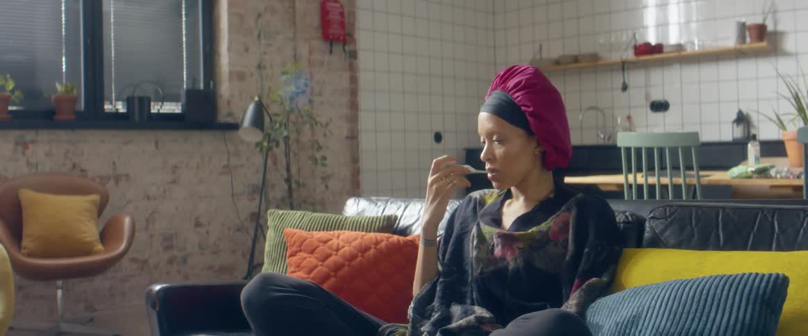 A woman taking her temperature while sitting on a living room sofa