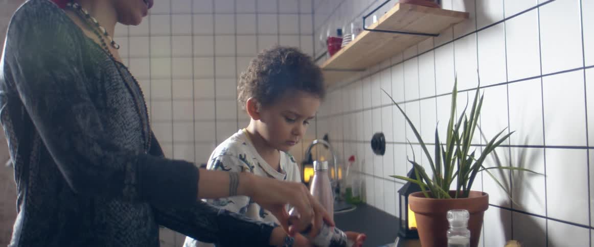 A woman and a boy in a kitchen preparing food with a wall and sink in the background
