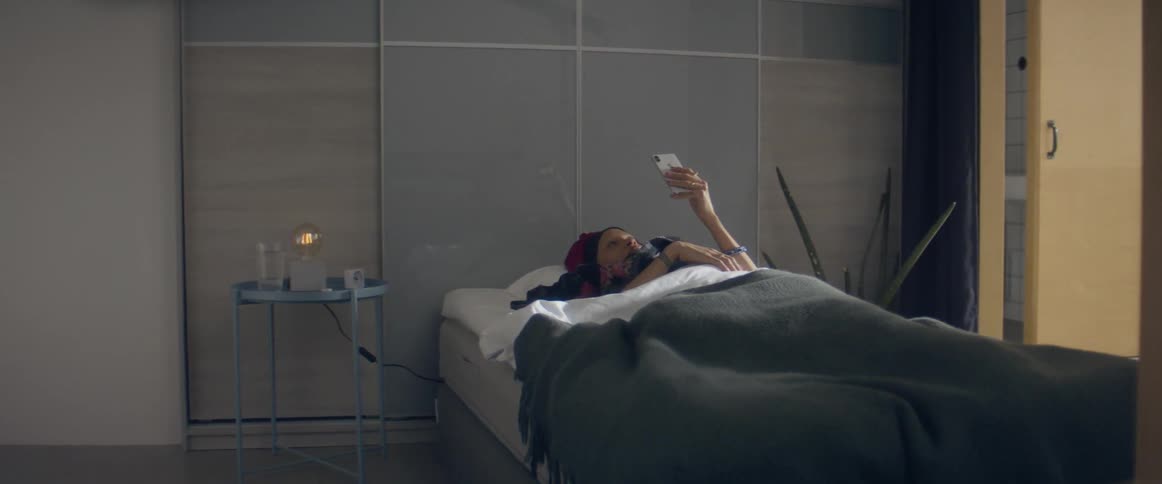 A woman lays in bed while holding her phone up above her
