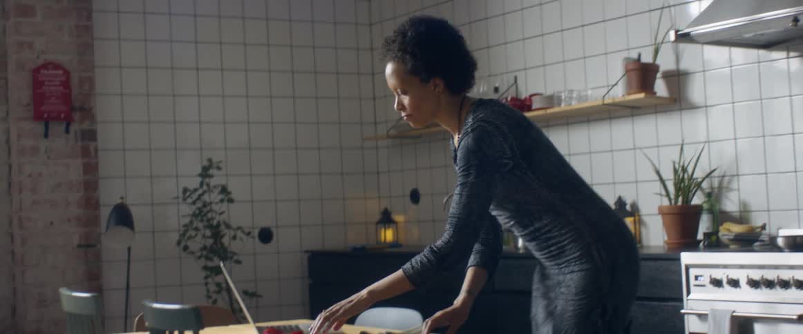 A woman at home dances as she looks at her laptop and chops vegetables