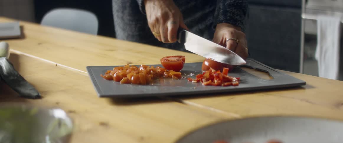 A woman dances while cutting a tomato in a home kitchen during the day