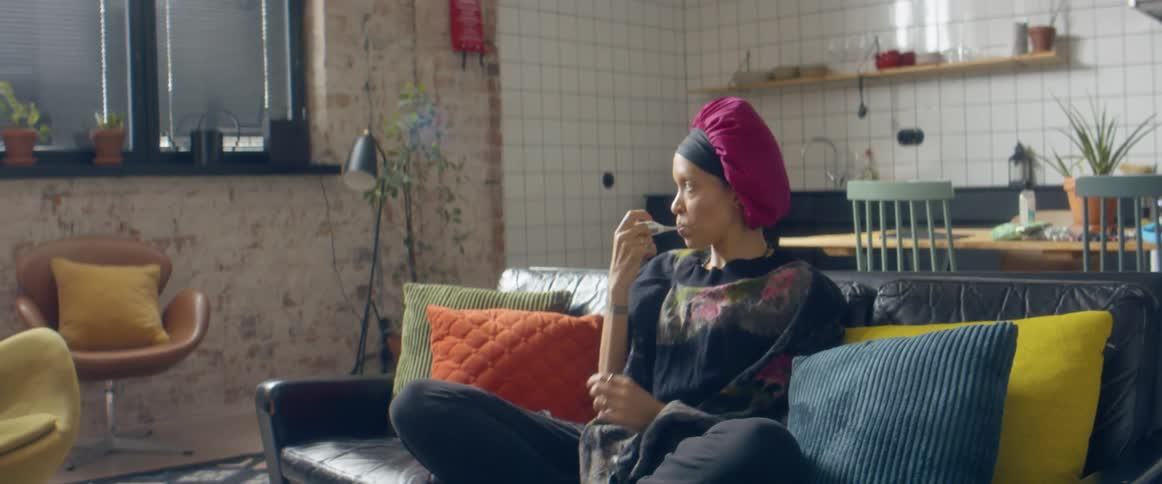 A woman at home sits on the couch and takes her temperature