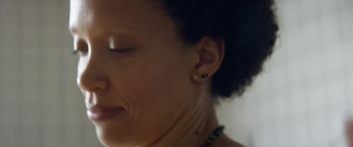 A woman with a necklace in a room dancing with a wall in the background