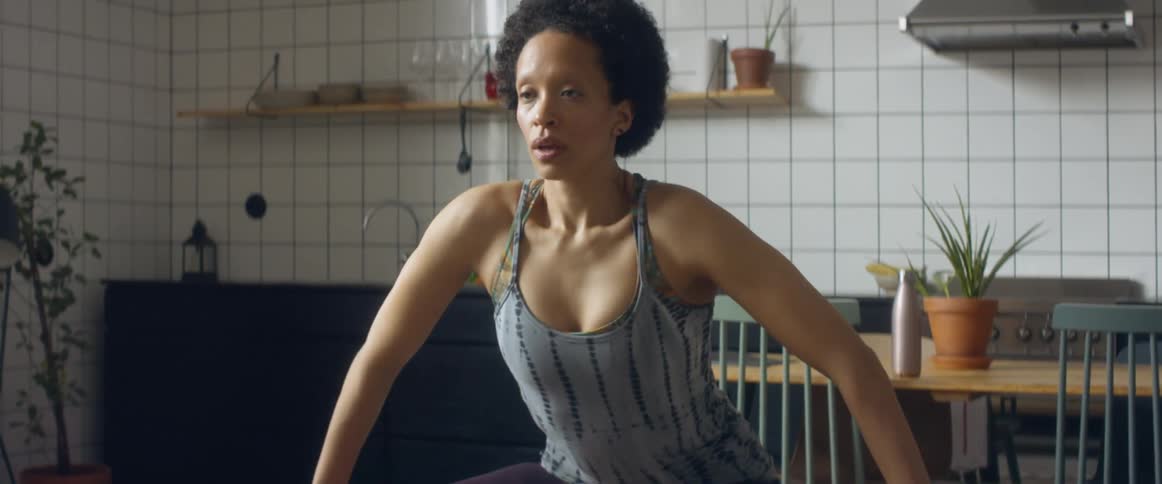 A black female in the kitchen stretching and squatting in the kitchen area