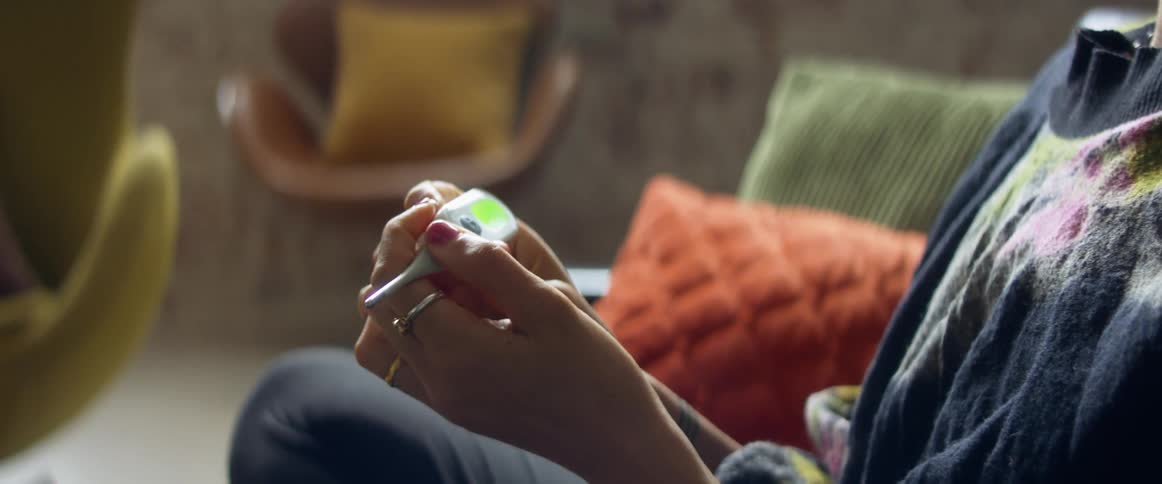 Woman sitting in a couch at home checks her temperature with an oral thermometer