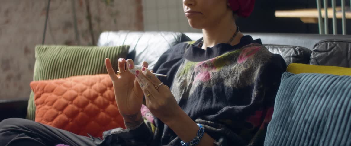 A woman at home sits on her couch and takes her temperature