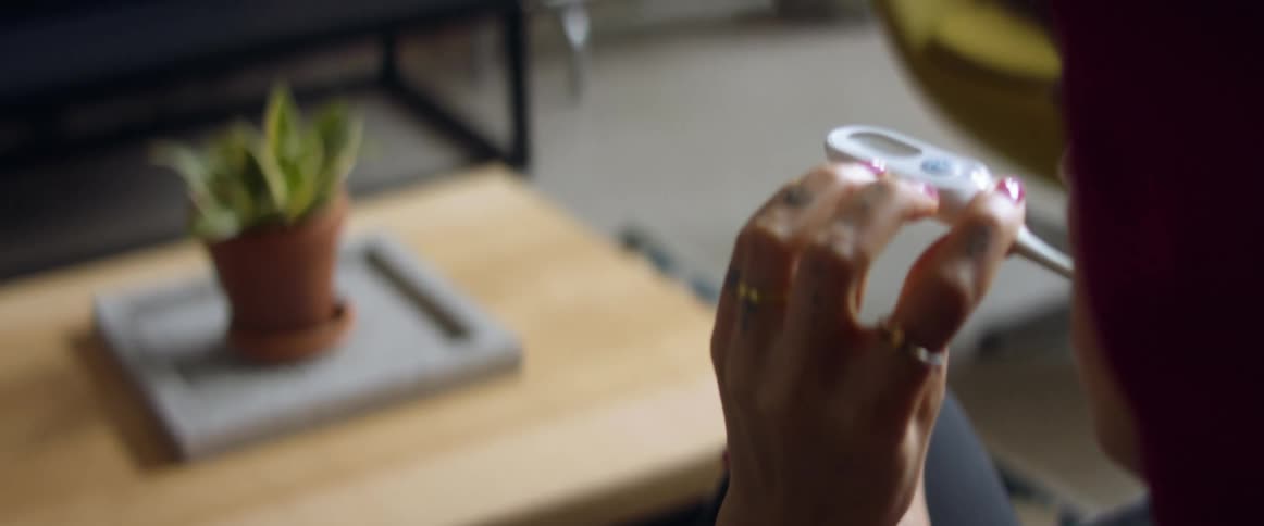 A woman sitting on a couch in a room next to a table looking at a thermometer