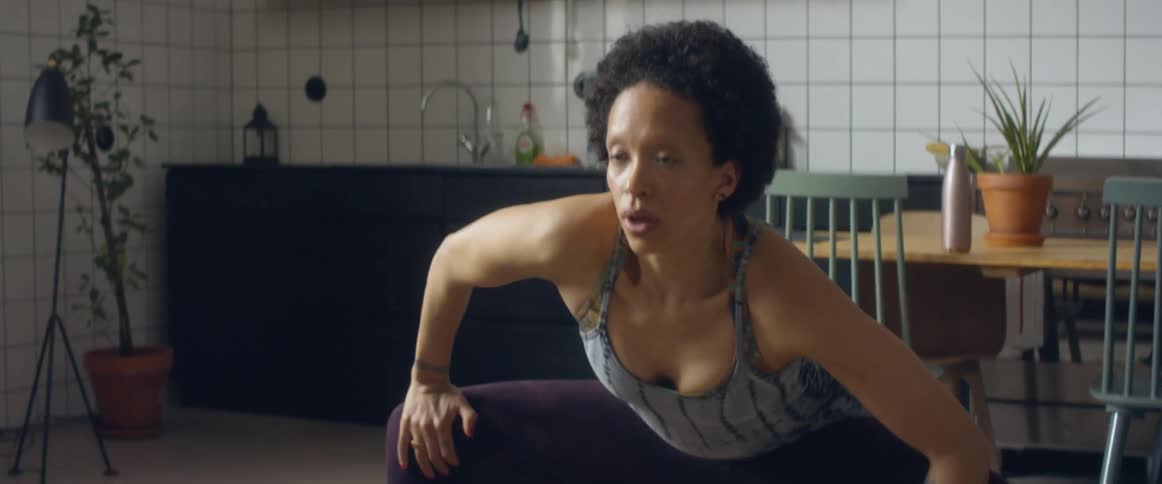 A woman in a tank top exhaling while stretching at home