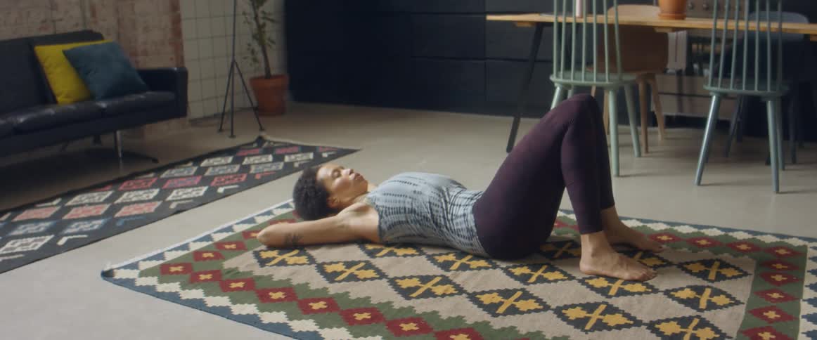 A woman lies on a rug at home with her eyes closed