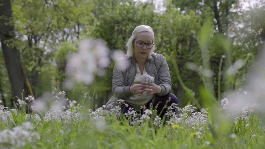 Woman sitting in a meadow quietly gathering wildflowers in a peaceful moment.