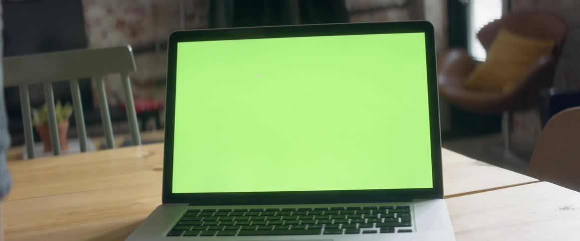 A woman stands at her kitchen table while typing on her laptop and walks away
