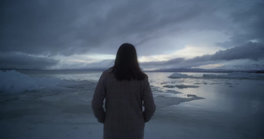 Woman wearing a coat walkin over the ice on a frozen lake at sunset