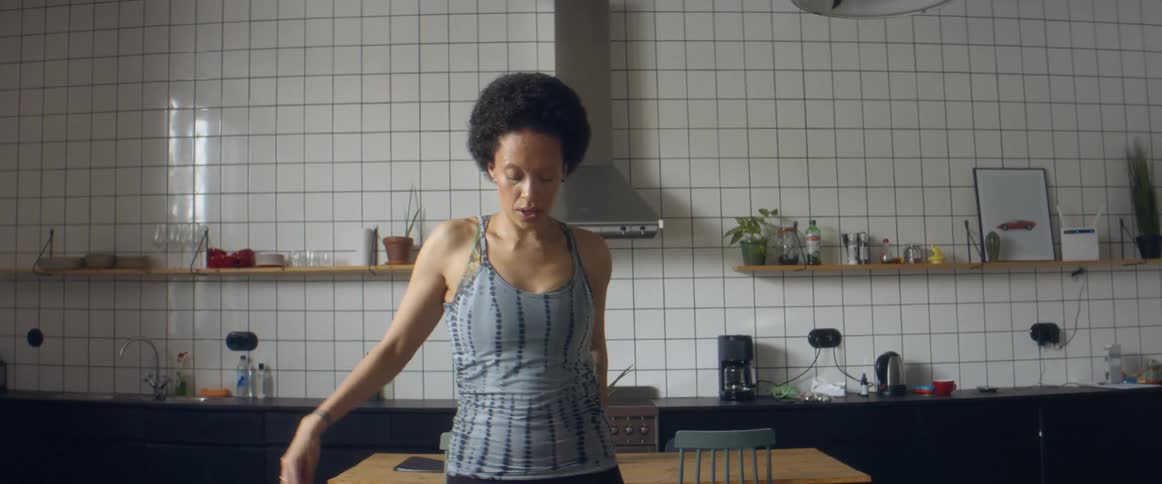 A woman stands on a rug and stretches her arms and legs in front of her kitchen table