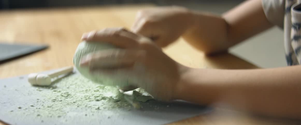 A little boy sits at a table and carves into a light green mold of dry clay