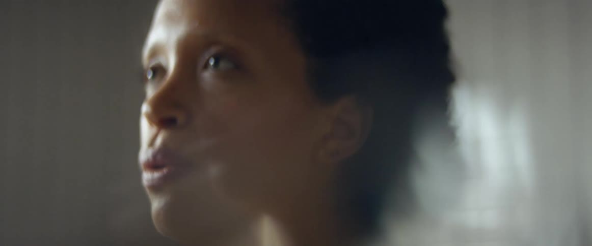 A black female from the neck up is talking and breathing hard in a room