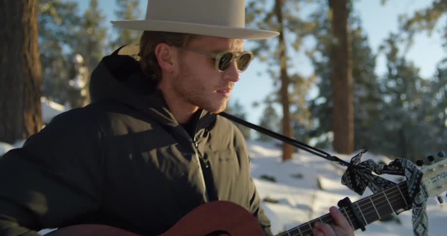 A man stands in a forest and sings and plays his guitar