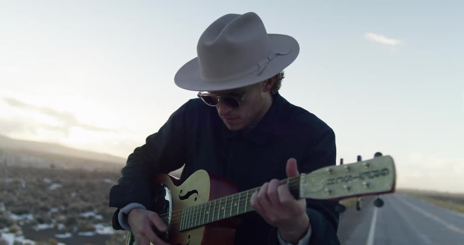 A man playing an acoustic guitar next to a paved rural road