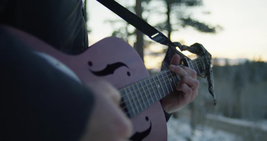 A man playing a resonator guitar outdoors at sunset