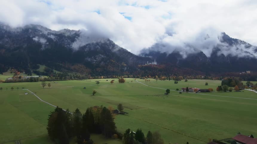 Aerial view of a small rural town in the green fields near the cloud covered mountaintops