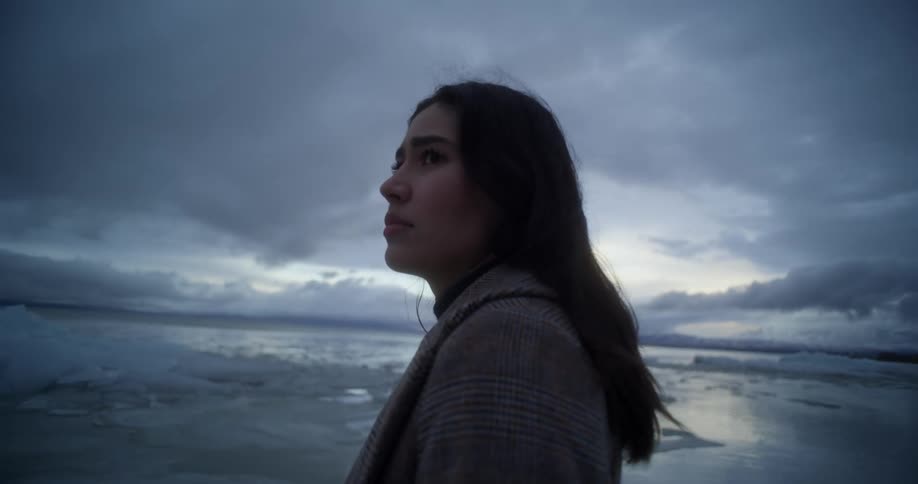 A woman standing on a beach with the ocean sky and clouds in the background