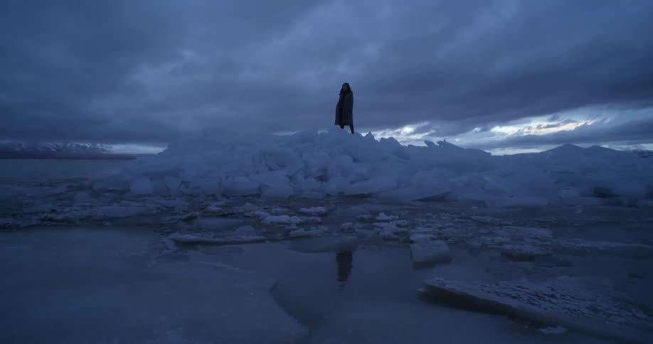 Silhouette of a woman standing over a pile of ice on the coast of a lake near the mountains