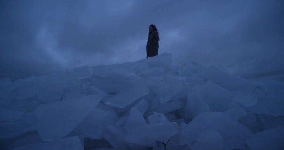 A woman is standing on a pile of large ice chunks