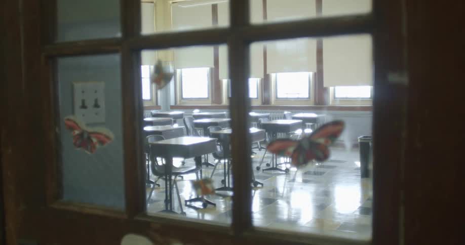 Rolls of desks in a school classroom seen through the window on the classroom door