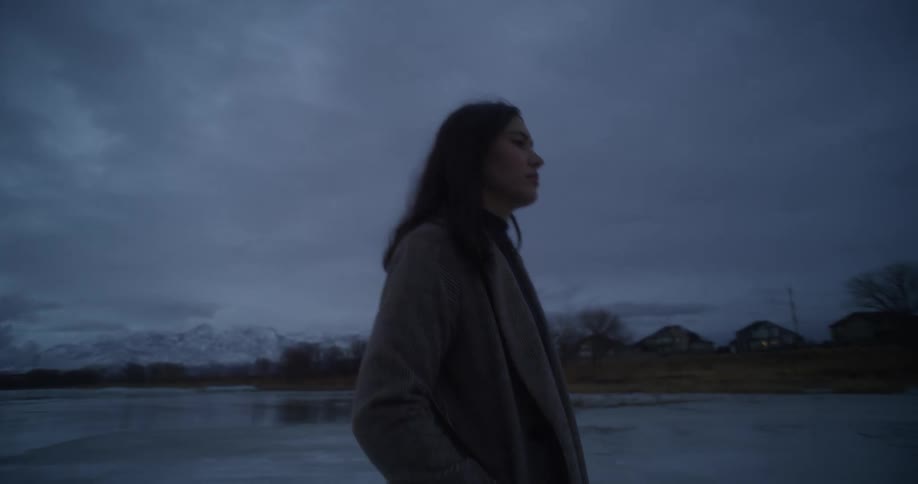 A woman in a coat walking alone on a beach at dusk