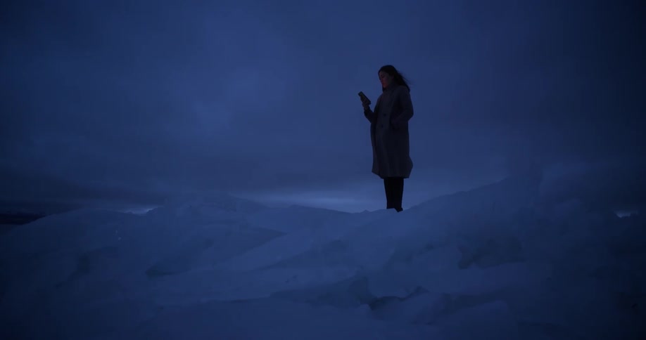 A woman takes out her smartphone as she stands on an ice glacier at night