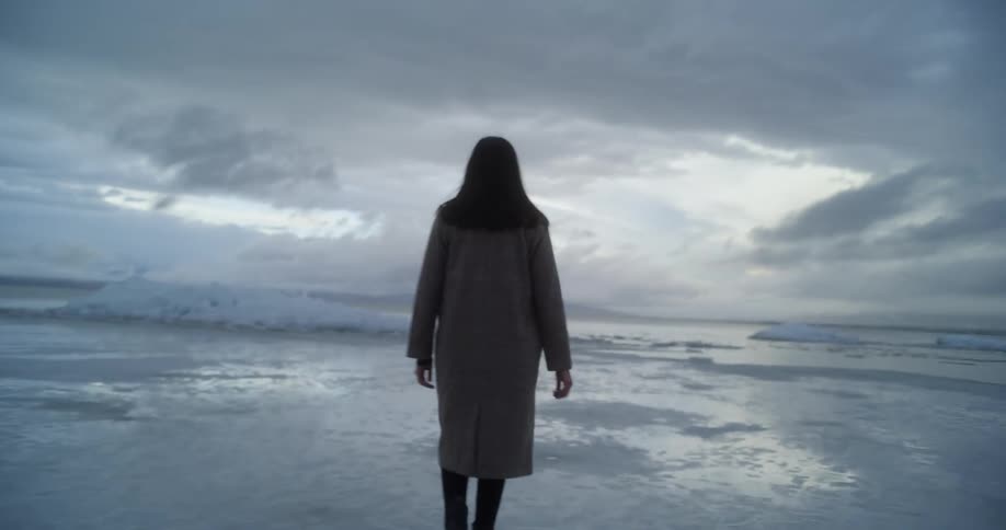 Silhouette of a woman walking on the frozen surface of a lake at evening
