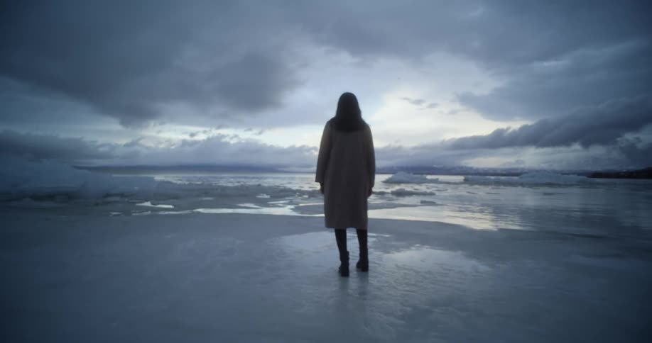 Silhouette of a woman standing on the frozen coast of a lake at sunset