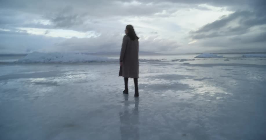 Woman walks across ice that reflects sky and stretches to the horizon