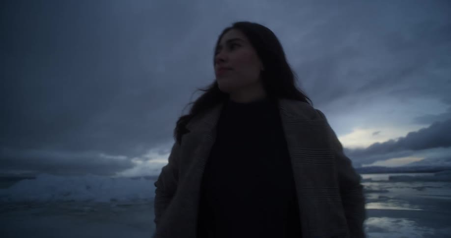 A woman walking away from a body of water with ice caps in an artic area at sunset