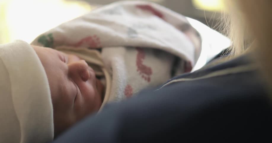 Blonde woman gently rocks sleeping baby swaddled in blanket