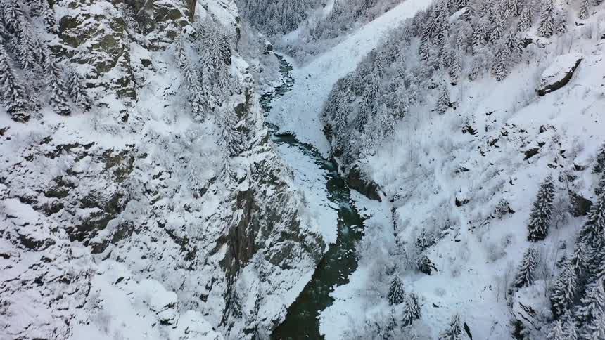 A river runs through a narrow valley in a snowy mountain range during the day