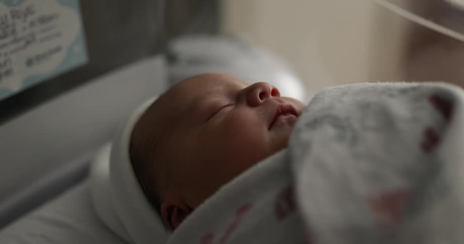 A baby with a hat and blanket sleeping in a plastic cradle