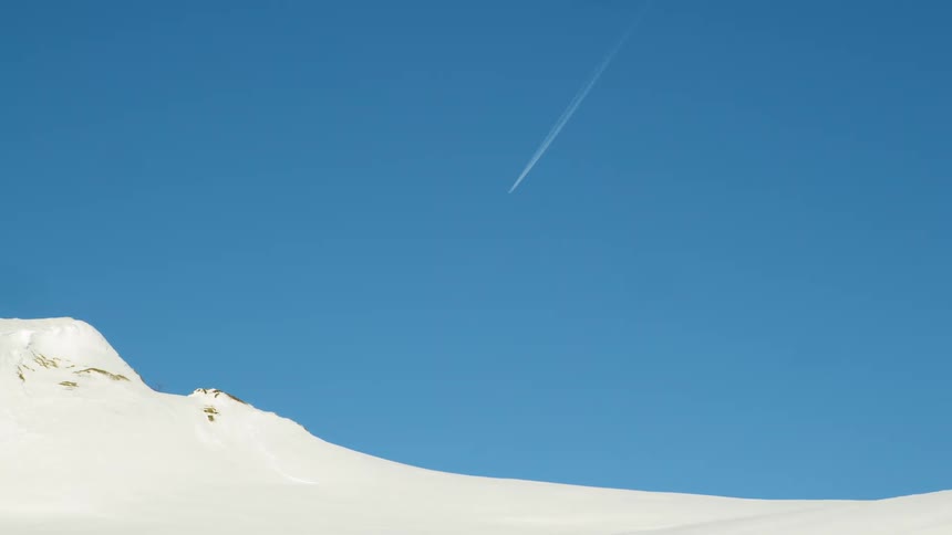 Jet move through deep blue sky over snow blanketed mountains leaving contrail