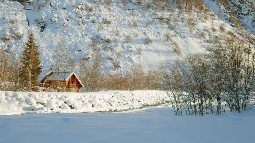 A river flows in front of a cabin in a snowy rural area