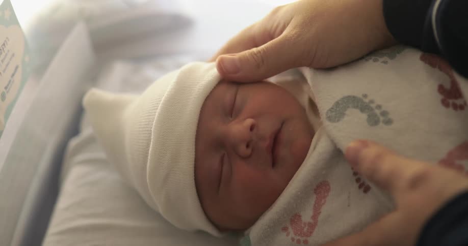 Person adjusts cap on sleeping infant stroking childs cheek