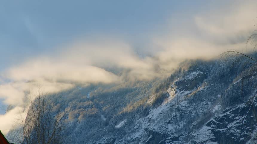 A landscape with trees and a mountain range with the sky and clouds in the background