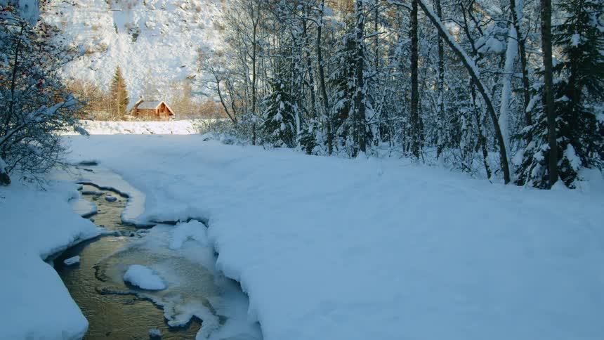 Forest and icy stream remain in shadow while house near slope sites in sunlight