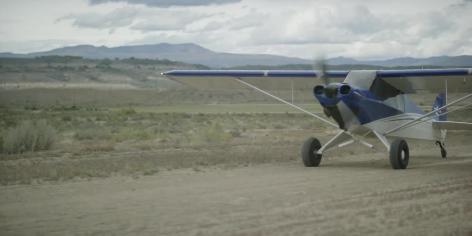 A single-engine plane taxis down a dirt runway during the day
