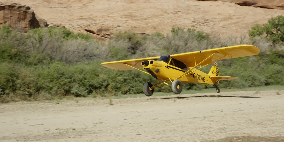 A yellow plane slowly moves down a dirt field