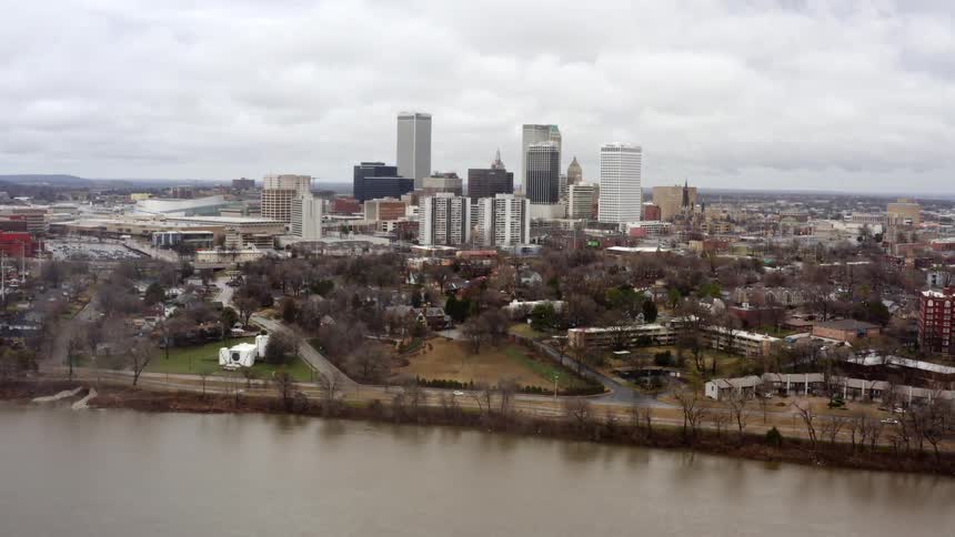 A city skyline near a river with buildings and trees with the sky and clouds in the background