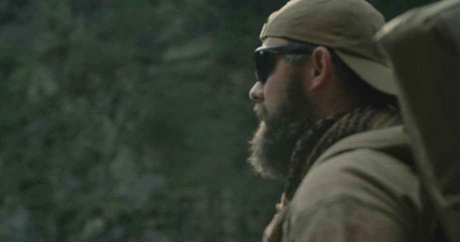 Bearded man carrying backpack hikes through wilderness