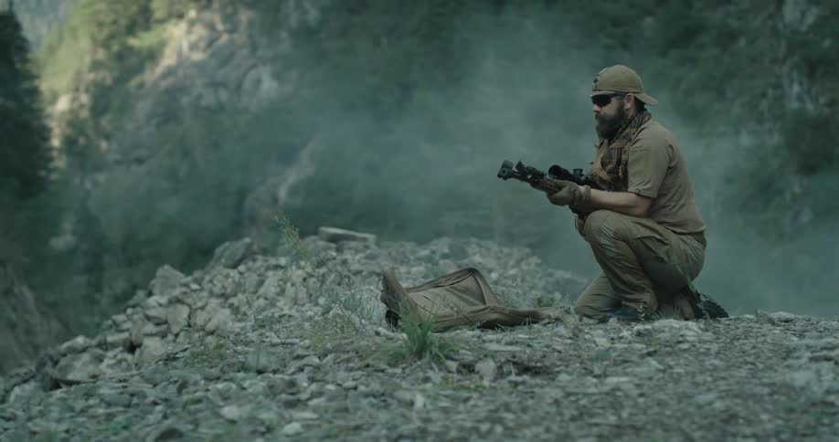 A man with a hat and sunglasses taking up a rifle from a bag