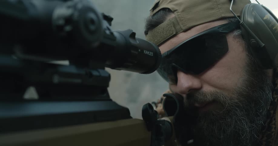 A man with a hat and sunglasses aiming a rifle with a scope